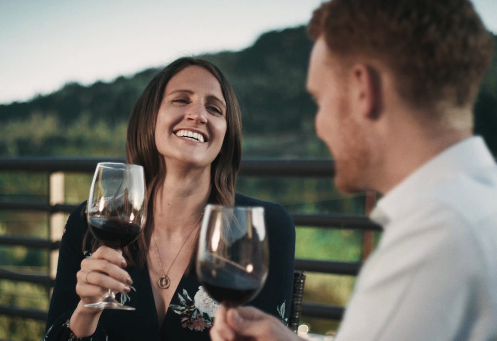 A woman and a man smile as they enjoy a glass of red wine.