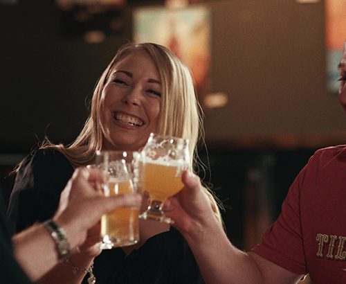 Two men and a woman laugh while toasting with beers.