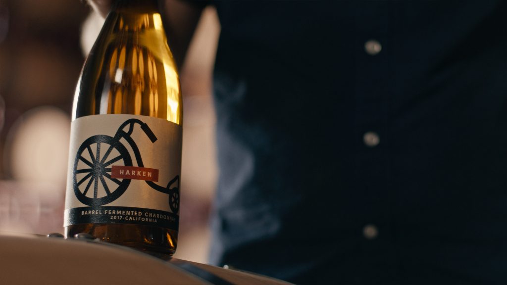 A close-up of a Harken Barrel Fermented Chardonnay 2017 California wine bottle with a vintage-style label, set against a blurred background.