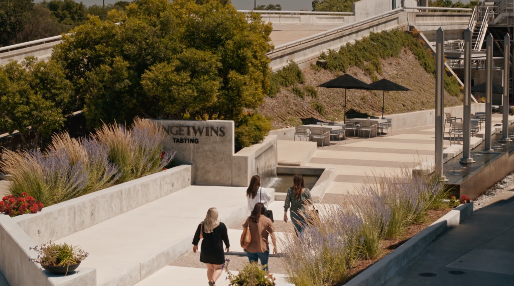 LangeTwins Winery Case Study Photo 3 Four people walk towards the 'LangeTwins Tasting' area, surrounded by ornamental grasses. Tables with umbrellas are set up in the background, creating an inviting outdoor space.
